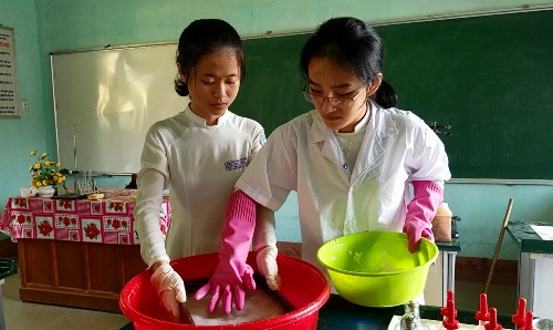 Hai nữ sinh thực hiện công đoạn sản xuất giấy theo phương pháp thủ công trong phòng thí nghiệm. Ảnh: Võ Thạnh